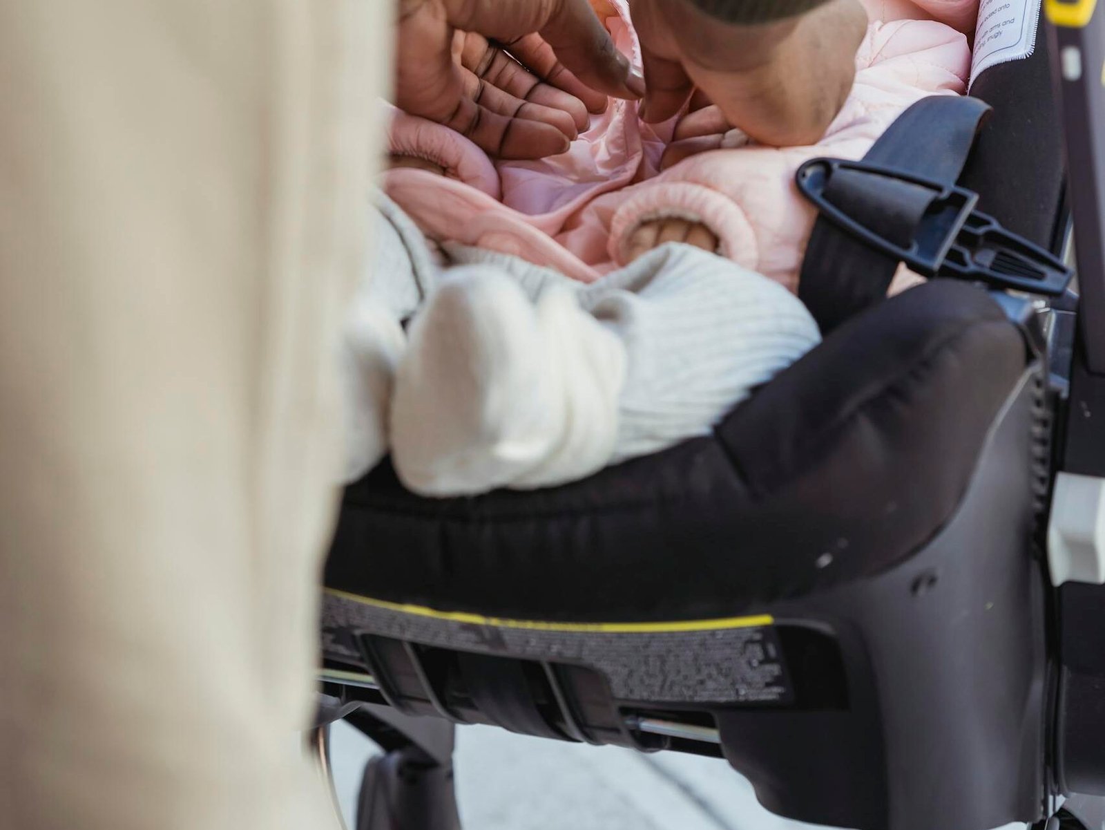 Crop unrecognizable African American father buttoning clothes on infant lying in comfy baby carriage on street